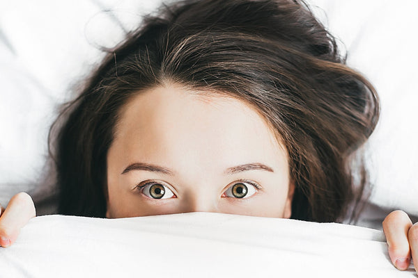 Woman pulling a blanket up over her face in a soft, dim bedroom