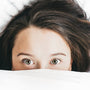 Woman pulling a blanket up over her face in a soft, dim bedroom