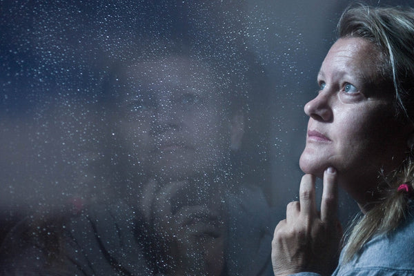 Woman resting her hand against her jaw by a rain-flecked window