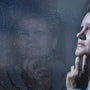 Woman resting her hand against her jaw by a rain-flecked window