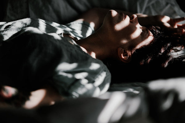 A woman resting in bed with her head on a pillow, striped light from the blinds falling across the room