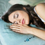 A woman sleeping peacefully in bed, resting on a soft blue pillow