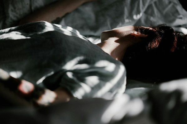 A person asleep under a grey blanket in a softly lit bedroom