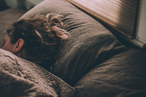 A person sleeping peacefully in bed as soft daylight comes through the window blinds