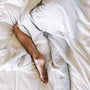 A person resting in bed under a soft white blanket