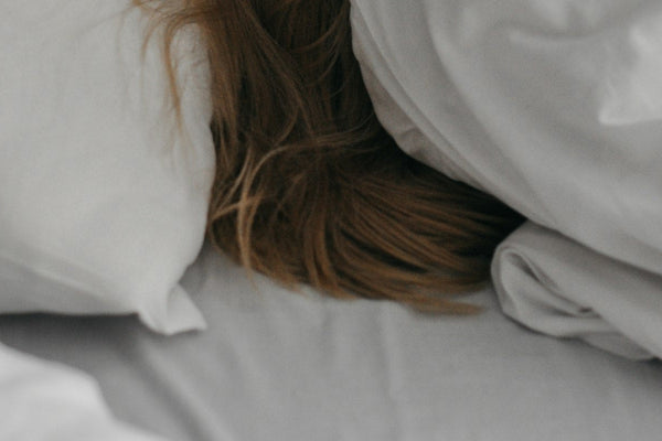 A woman pulling a grey blanket up over her face while lying in bed
