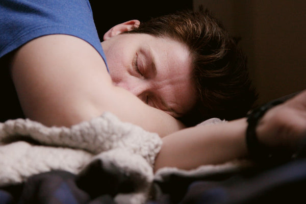 A person lying on their side in bed with soft morning light across the pillow
