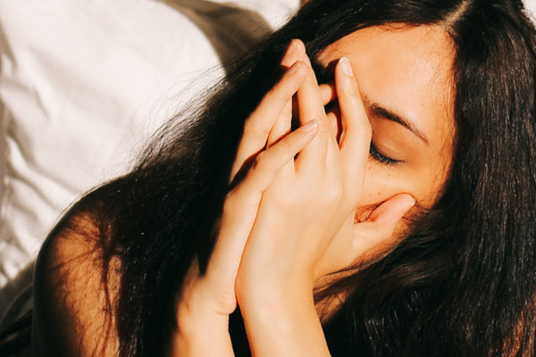 A woman lying in bed in soft morning light with her hands pressed over her face