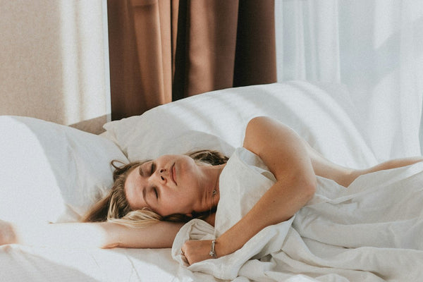 A woman lying calmly in a bed with white and grey sheets, eyes closed