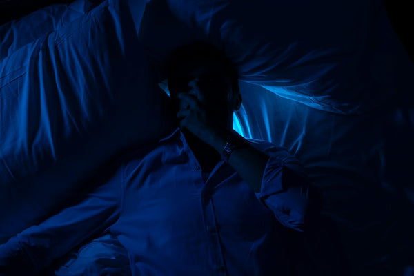 A person lying in bed in a dark bedroom with the covers pushed aside