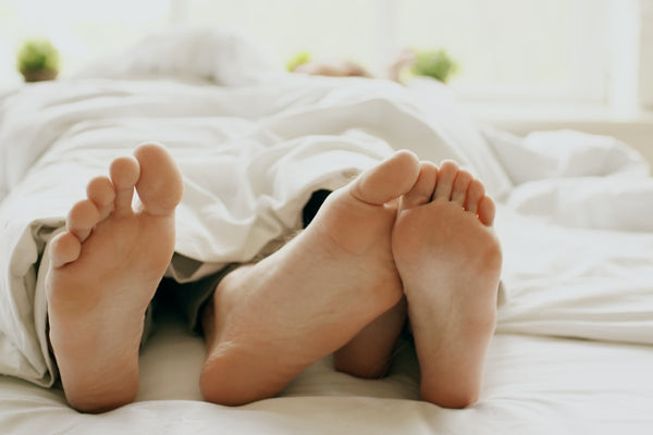 Feet peeking out from under a white duvet in a bright bedroom