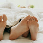 Feet peeking out from under a white duvet in a bright bedroom