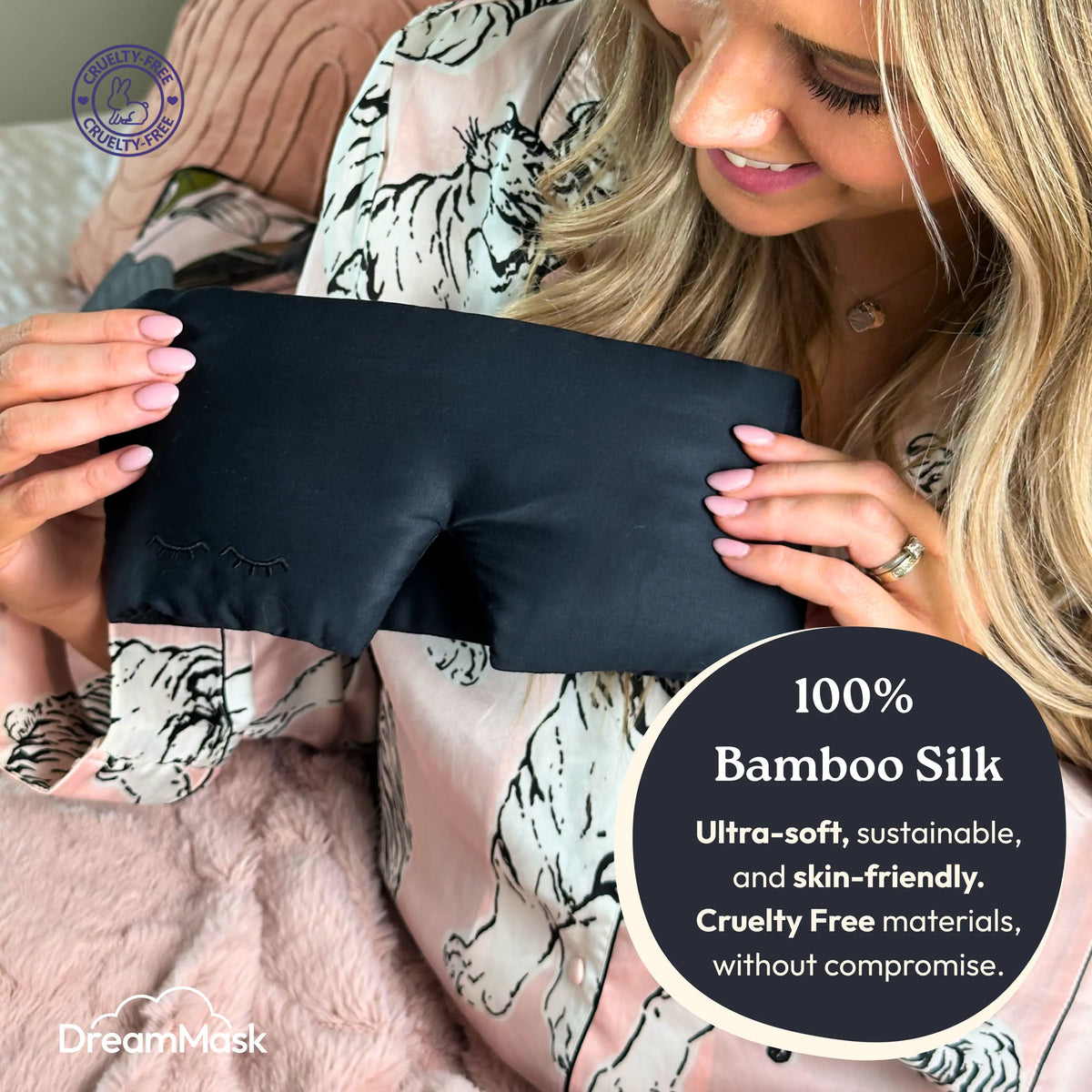 Woman holding a black bamboo silk eye mask with DreamMask branding.