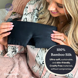 Woman holding a black bamboo silk eye mask with DreamMask branding.