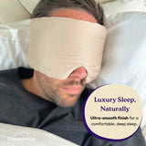 Man wearing a beige sleep mask with 'DreamMask' branding, lying on a pillow.