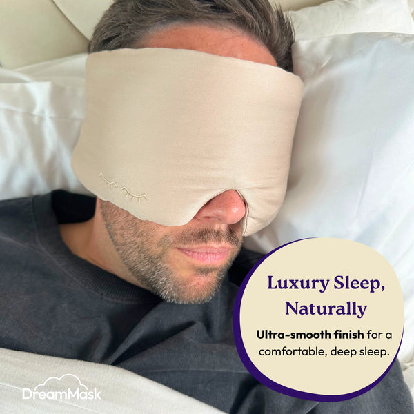 Man wearing a beige sleep mask with 'DreamMask' branding, lying on a pillow.