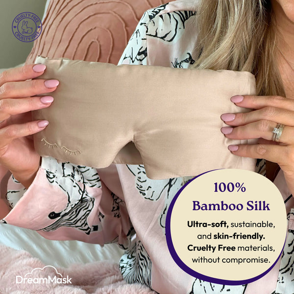 Person holding a beige DreamMask bamboo silk eye mask with product details.