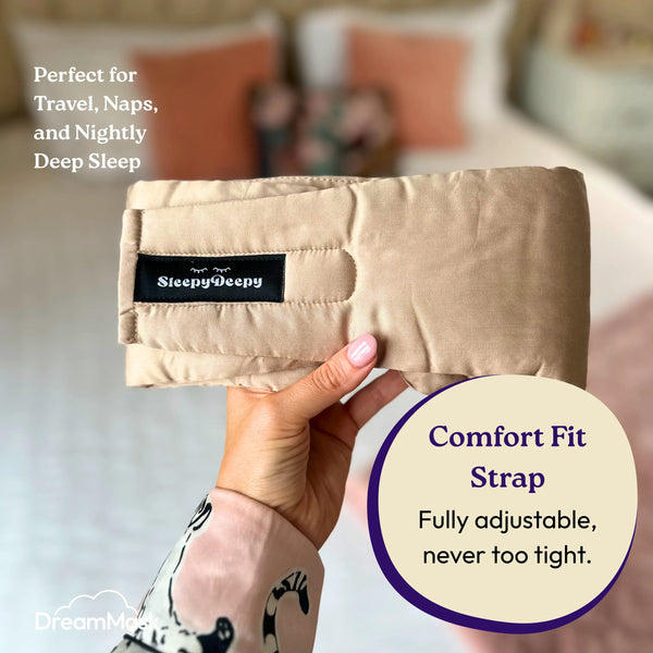 Beige travel pillow held by a hand with 'Sleepy Deepy' branding, set against a blurred bedroom background.