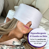 Woman wearing a white sleep mask with DreamMask branding, lying on a beige couch.