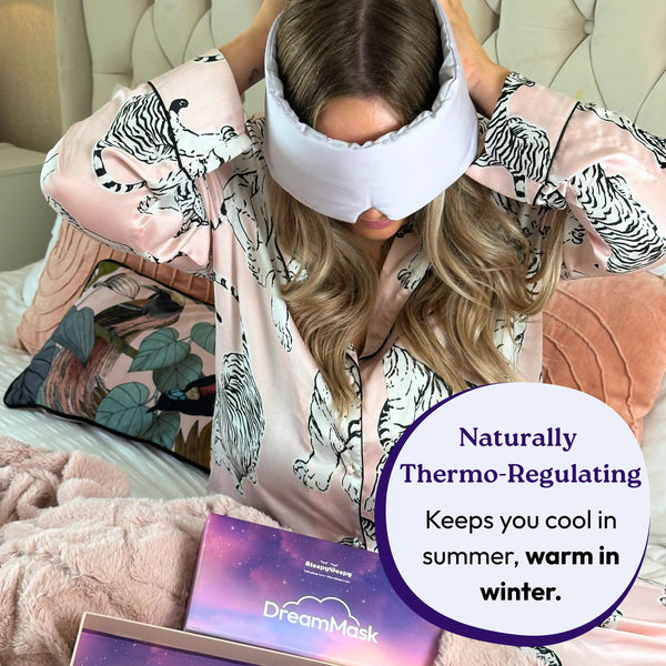 Woman wearing a patterned robe and white sleep mask, with 'DreamMask' packaging on a bed.