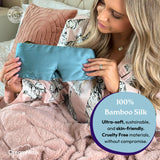 Woman holding a blue bamboo silk sleep mask in bed with text highlighting its features.