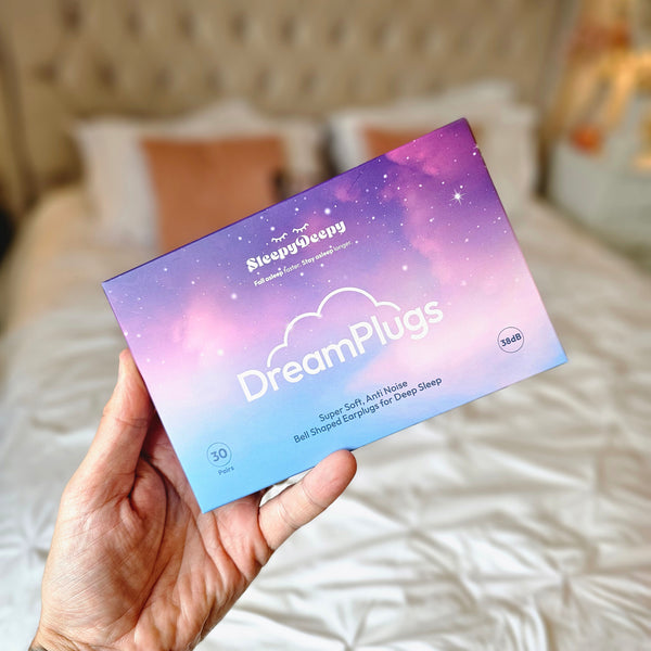 Hand holding a 'Dreamplugs' product packaging against a blurred indoor background